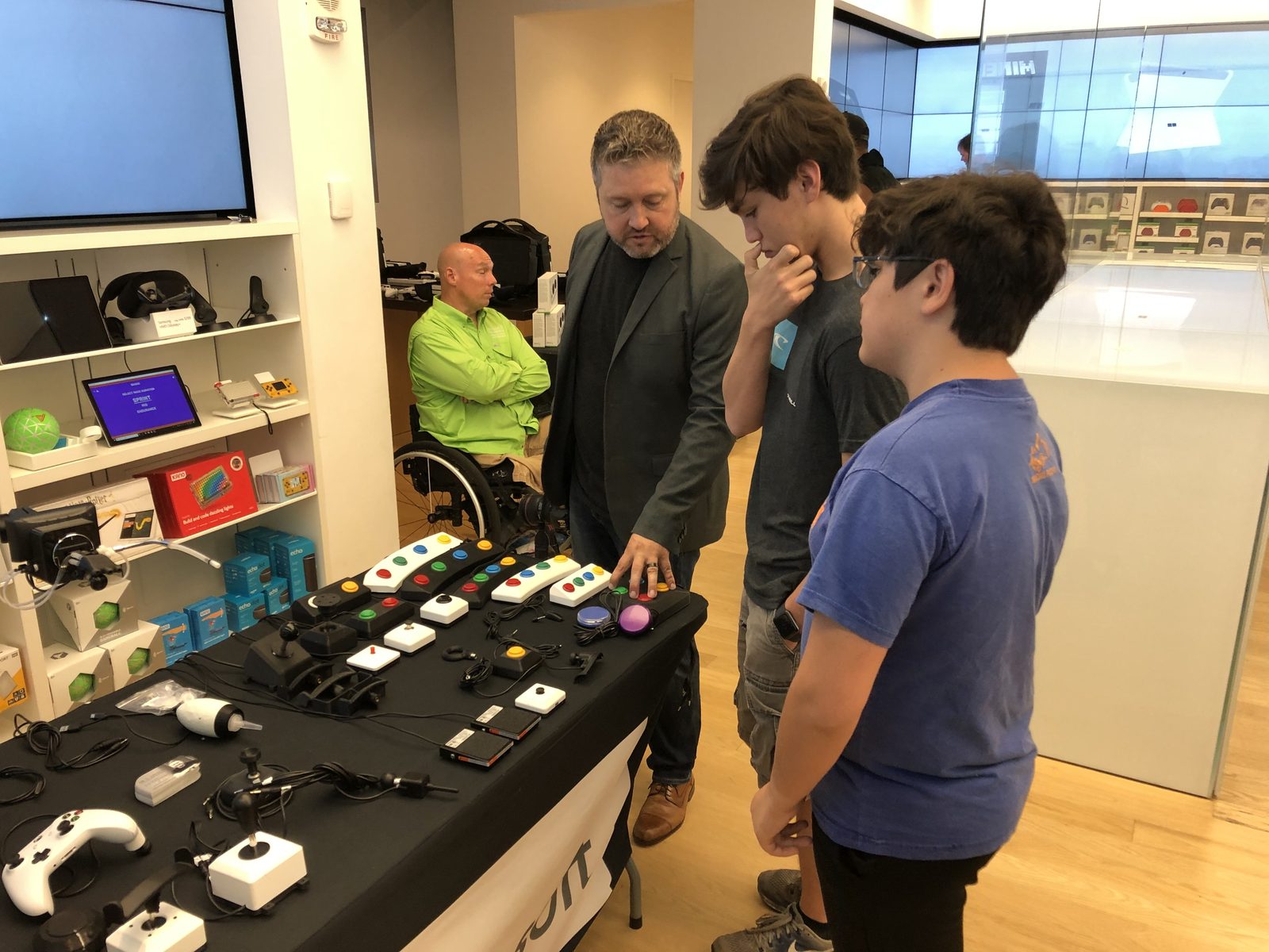 A table of adaptive gaming equipment — accessible button boxes, switches, joysticks, and controllers — at a Rehab Arcade event.