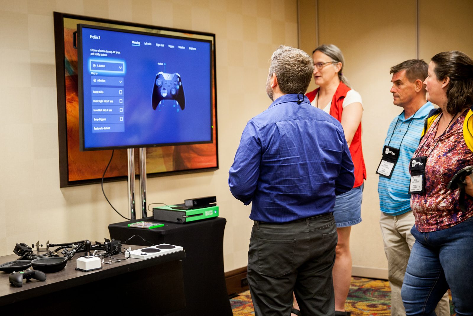 At a Rehab Arcade session, an occupational therapist shows a small group an adaptive-controller setup on a large screen.