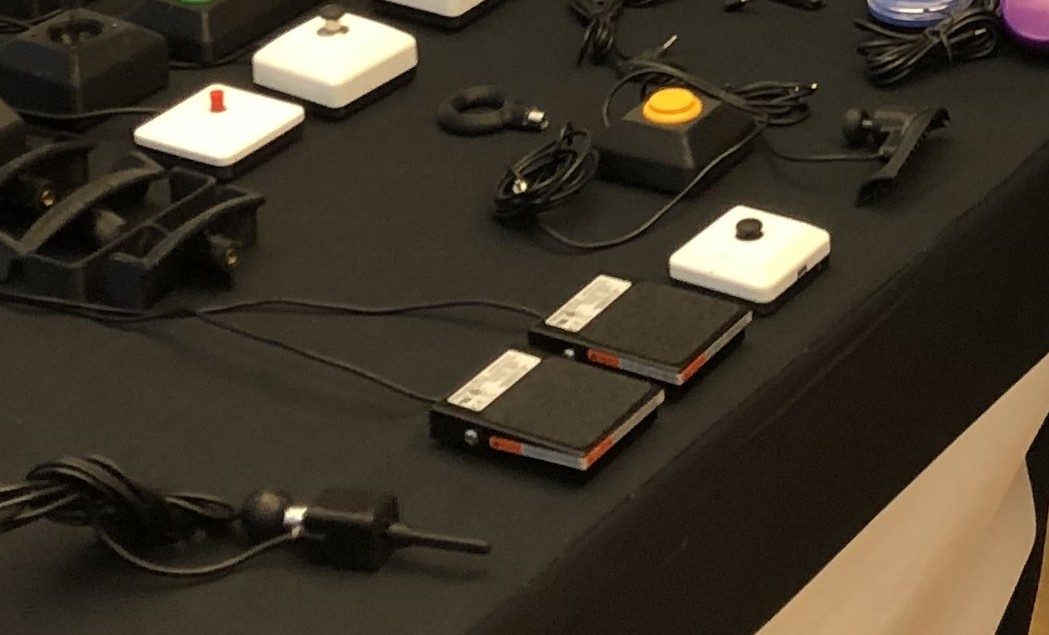 White adaptive switch boxes, small switches, and remapping hardware with cables arranged on an adaptive gaming demo table.