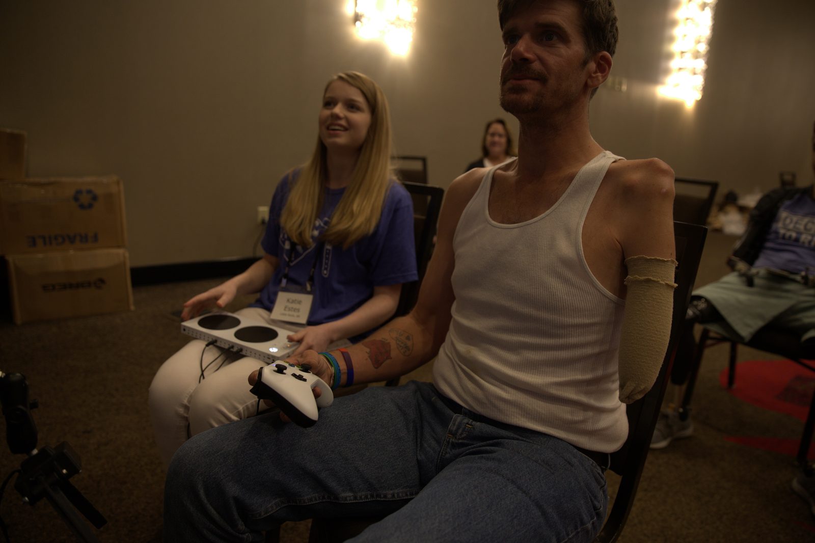An occupational therapist sits alongside a client during a one-on-one adaptive-gaming session, an Xbox Adaptive Controller resting on his lap.