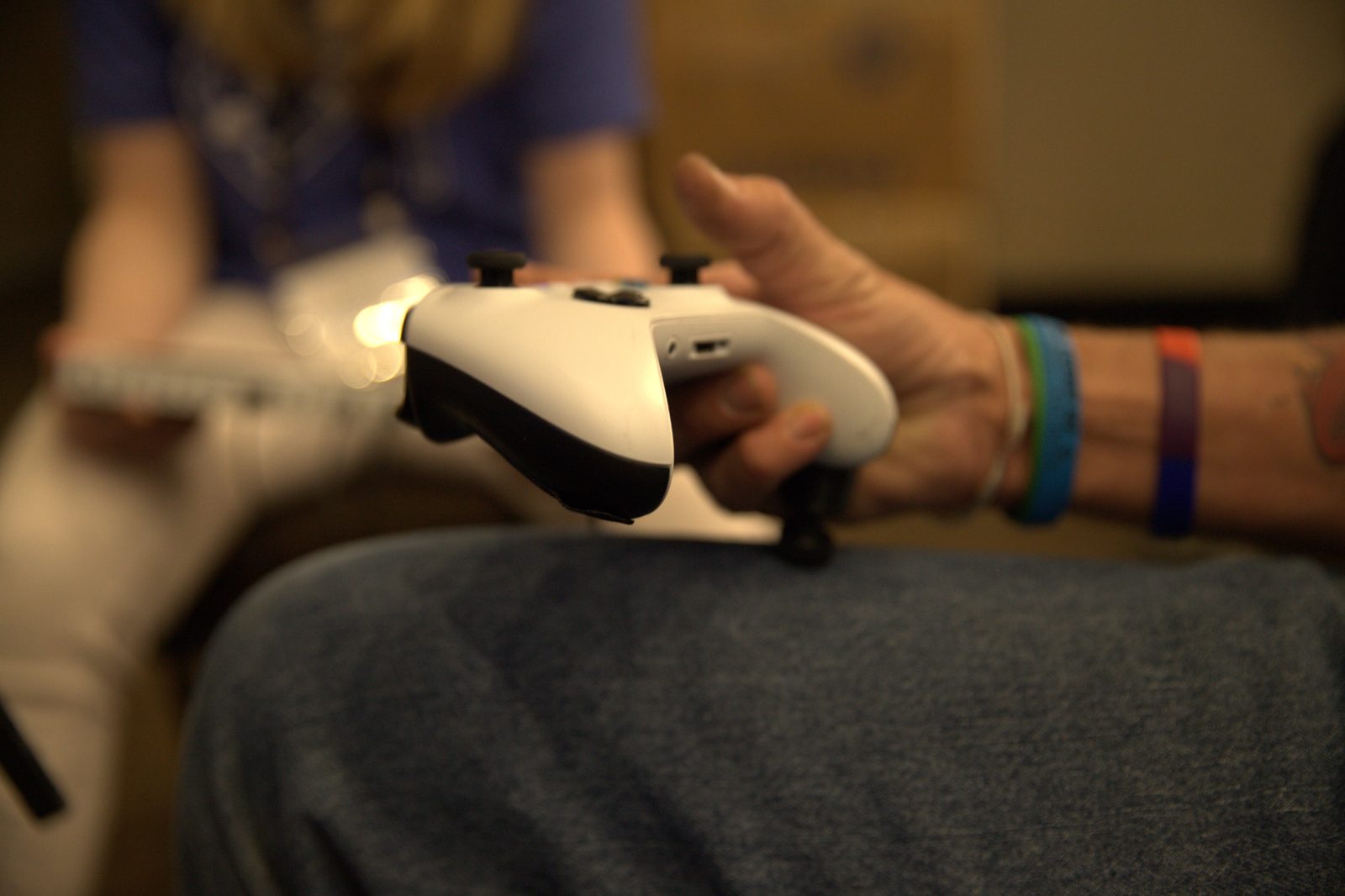 A client's hands resting on an Xbox Adaptive Controller during a therapy session, colored wristbands on one wrist.